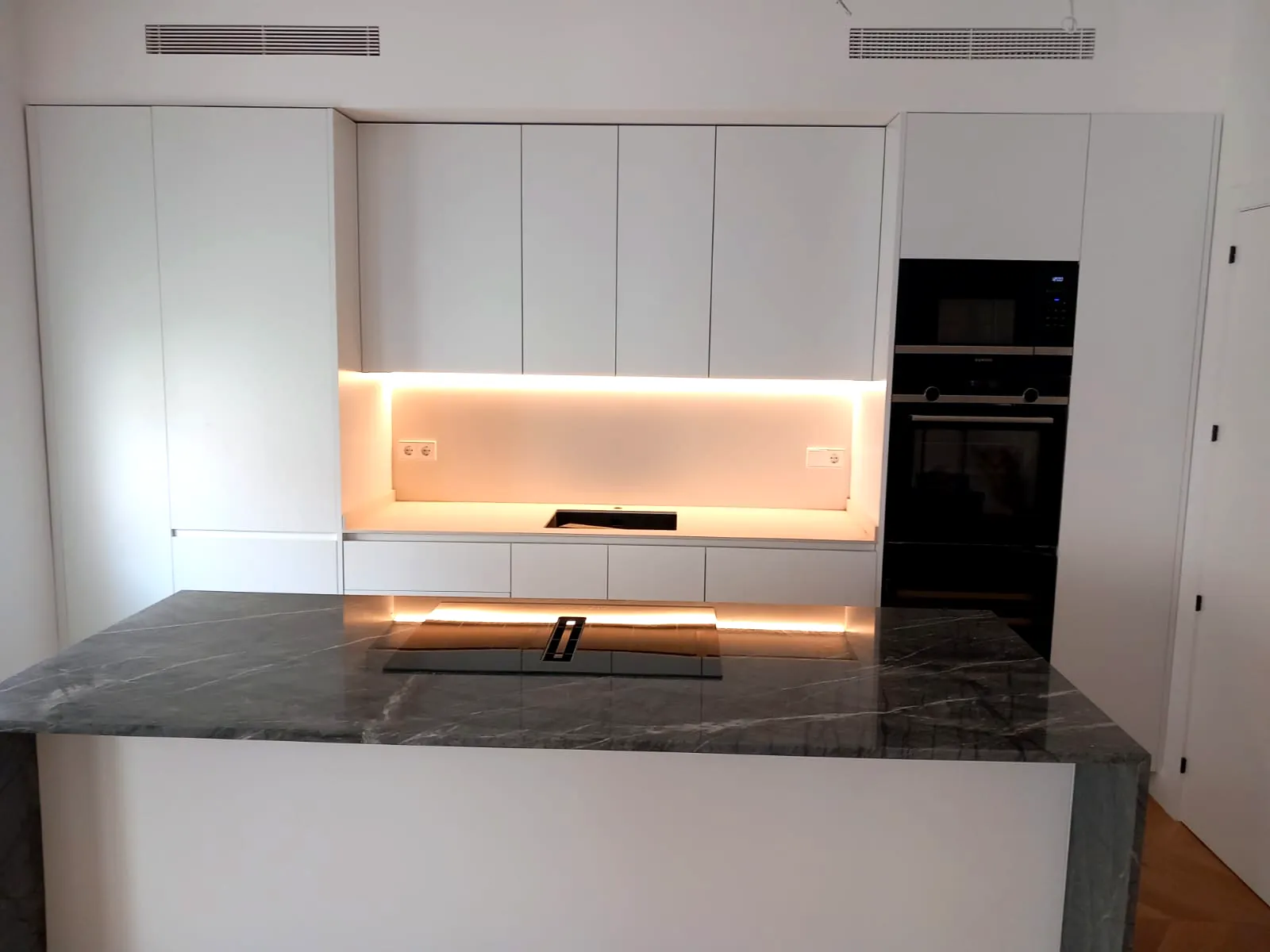 Cocina moderna blanca con isla de mármol oscuro e iluminación LED